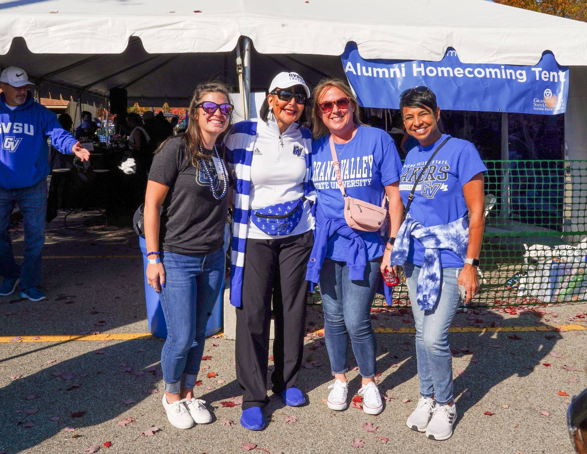 A group of alumni smile with President Mantella during a Homecoming tailgate wearing GV gear